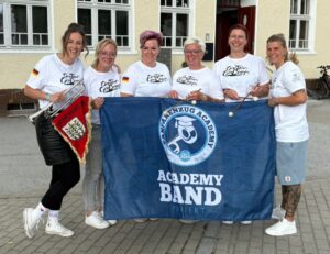 6 Mitglieder des Fanfarenzugs Hoyerswerda posieren vor der Flagge der Academy Band 2026